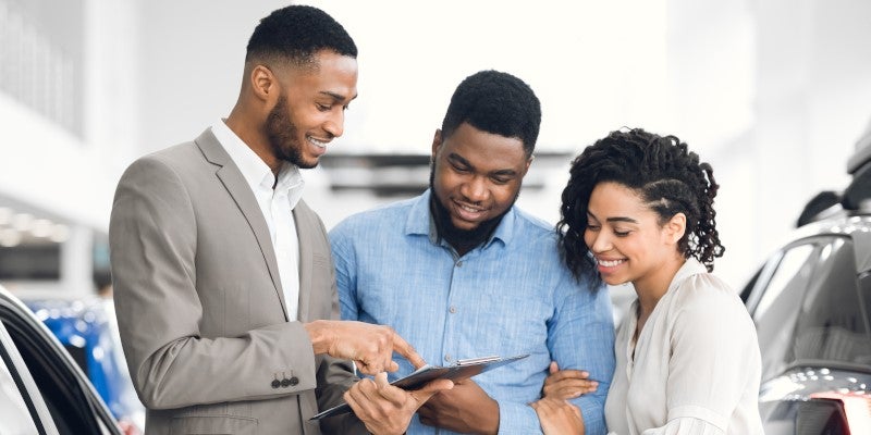 A couple shopping at a car dealership with a salesperson