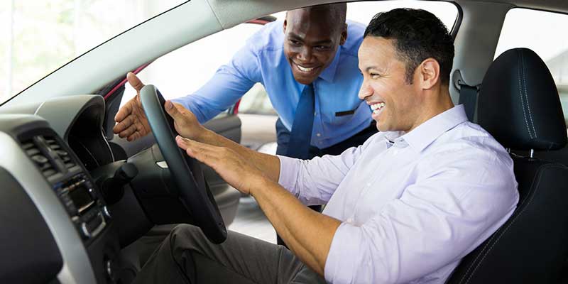 A man in his new vehicle's driver's seat with a salesperson outside the window